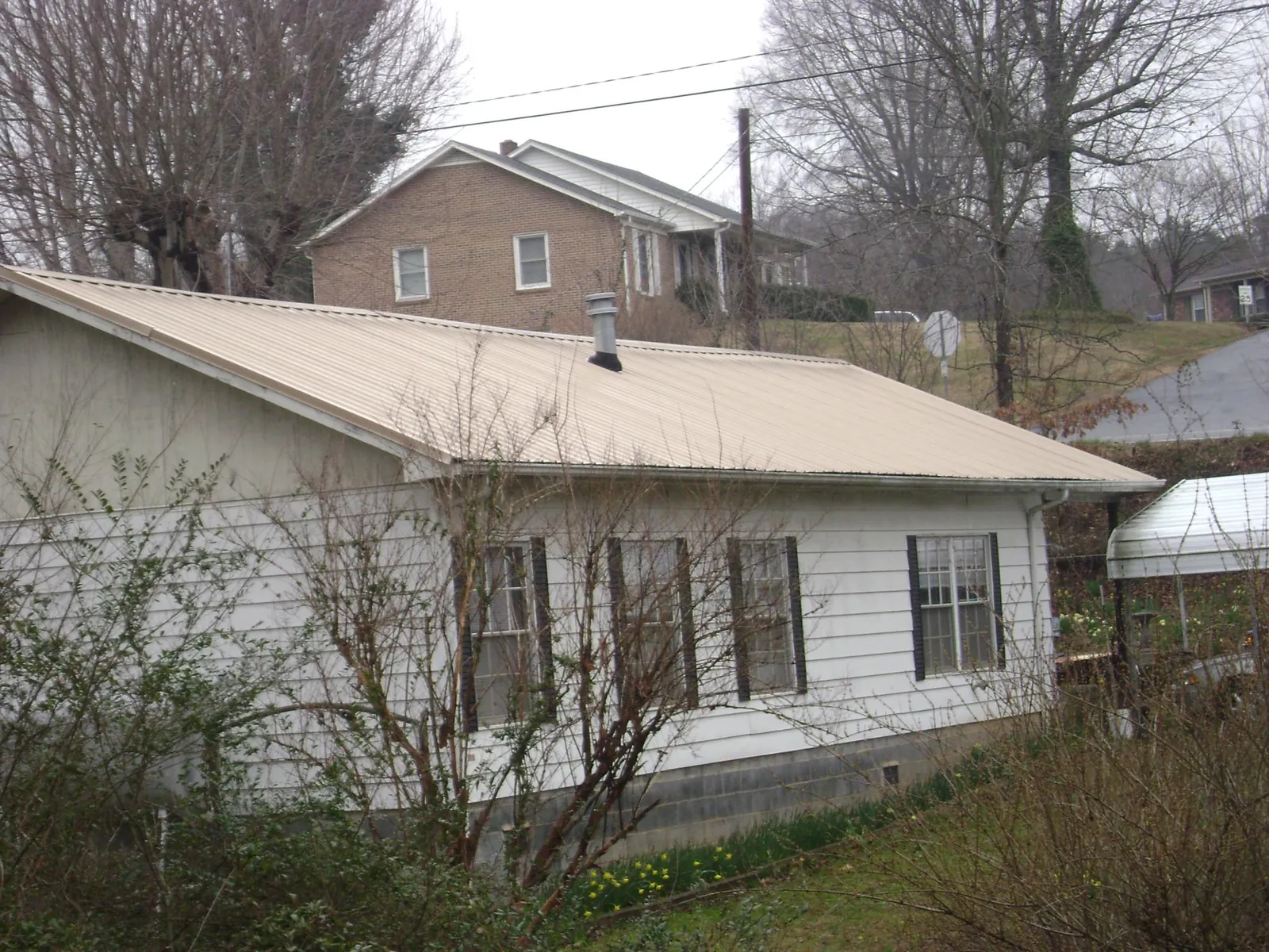 Tan metal roof on a white sided house set into a hillside — Commercial Roofing by Roofing Brothers in Blue Ridge Summit